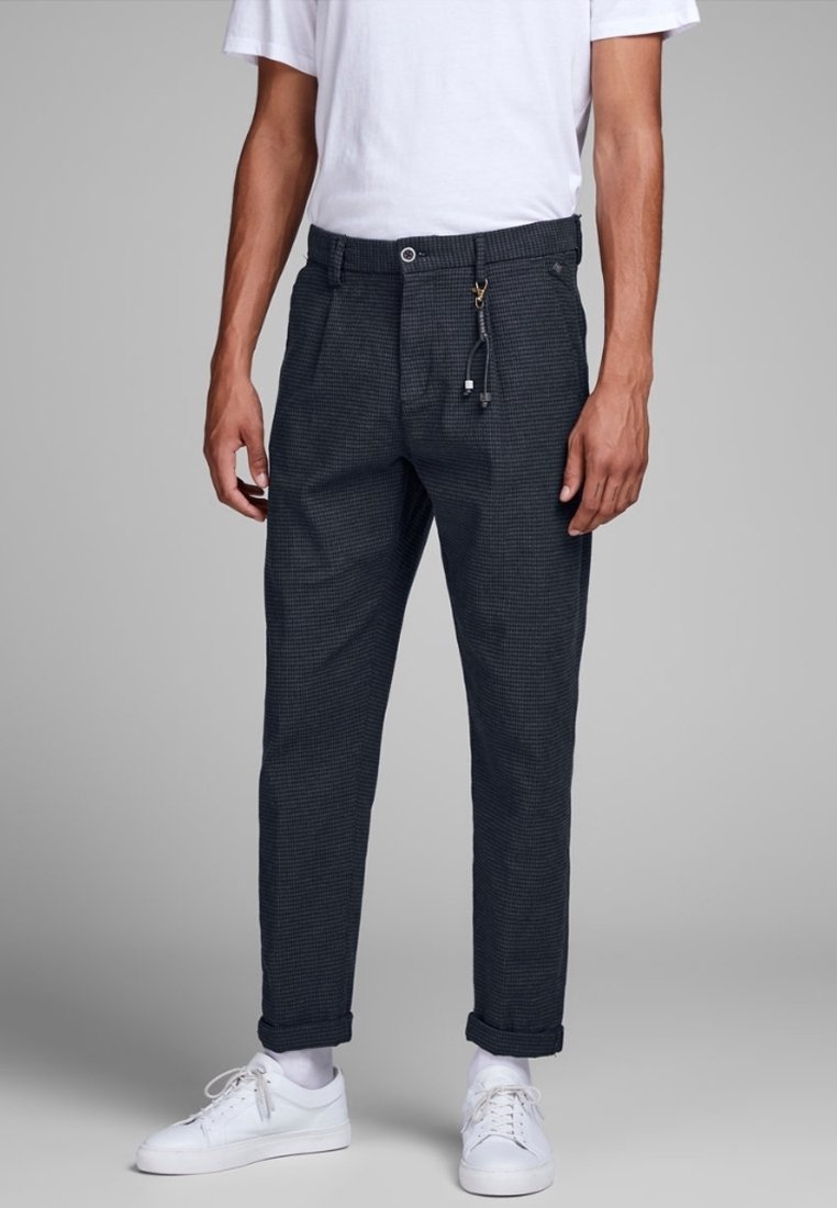 Mörka rutiga byxor med dragsko i midjan, sidofickor och uppvikta muddar, matchade med vita sneakers och en enkel vit t-shirt.