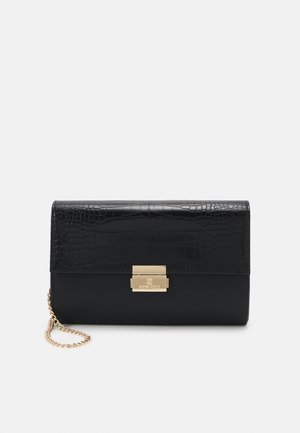 Czarna skórzana kopertówka z fakturowaną klapą, złotym prostokątnym zapięciem i krótkim złotym łańcuszkiem, na jednolitym jasnym tle.