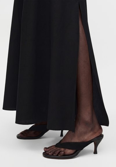 Άτομο που φοράει μαύρα σανδάλια με τακούνι και σταυρωτά λουράκια και μακριά μαύρη φούστα με πλευρικό σκίσιμο, που αφήνει ακάλυπτα τα πόδια και τα κατώτερα μέρη των ποδιών.