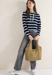 Sweat à capuche à manches longues rayé bleu marine et blanc, jean gris à jambes larges, tenant un sac fourre-tout en tissu doux vert olive avec une poche à l'avant.