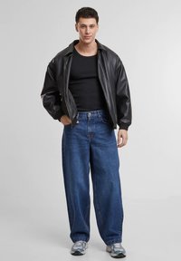 Μαύρο δερμάτινο μπουφάν τύπου bomber με ριμπ μανσέτες, φορεμένο πάνω από εφαρμοστό μαύρο τοπ χωρίς μανίκια. Χαλαρό μπλε τζιν και γκρι αθλητικά παπούτσια ολοκληρώνουν το σύνολο.