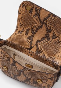 Ruskea ja musta serpenttiininahkakuosiset käsilaukku, jossa on kultainen magneettinappi ja beige vuori, jossa on vetoketjullinen tasku.