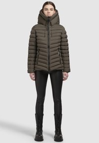 Apmantojama olīvzaļā jaka ar augstu apkakli un kapuci, ar rāvējslēdzēju priekšā, diagonālām šuvēm un divām rāvējslēdzēja sānu kabatām.