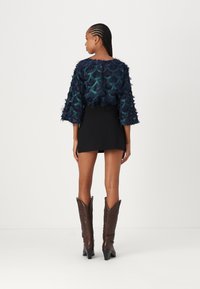 Blouse en voile navy avec un motif de textures vertes en écailles, manches trois-quarts, assortie à une jupe noire et des bottes de cowboy brunes à bout pointu.