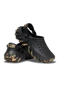 Schwarze Clogs mit Sohlen im Camouflage-Muster, ausgestattet mit Belüftungsöffnungen, verstellbaren Riemen und strukturiertem Gummi für Grip und Haltbarkeit.