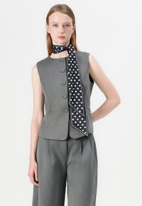 Gray tailored vest, sleeveless, with round neckline and five buttons. Features a black scarf with white polka dots tied at the neck.