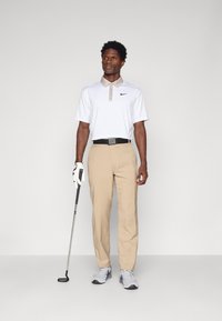 Camisa polo branca com colarinho bege, calças bege e sapatos cinzentos. Os acessórios incluem um cinto preto e um taco de golfe com uma luva branca.
