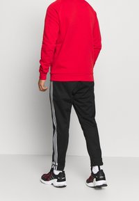 Červená mikina, černé sportovní kalhoty s bílými pruhy. Černé a růžové sportovní boty. Hladká tkanina, volný střih, žebrované manžety.