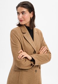 Houndstooth-patterned brown blazer with a notched collar, two buttons, and side pockets, made from a textured fabric.