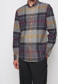 Herren Langarmhemd in Grau- und Dunkeltönen, mit einem karierten Muster und orangefarbenen sowie roten Akzenten. Mit Button-Down-Kragen und einer Brusttasche.