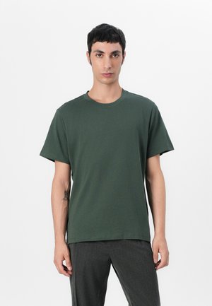 Camiseta de algodón verde oscuro con mangas cortas, cuello redondo y un corte relajado, mostrada sobre un fondo blanco.