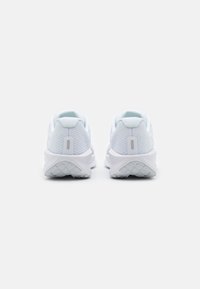 Une paire de chaussures de sport blanches vue de l'arrière sur un fond blanc uni, mettant en valeur des dessus en maille texturée et des semelles.