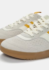 Sneakers aus hellgrauem Wildleder mit weißen Akzenten und gelben Streifen. Verfügen über runde Schnürsenkel, durchbrochene Details und eine Sohle aus Gummi.