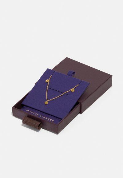 Gold necklace displayed on a purple felt background inside a dark brown box, featuring circular pendants and fine chain links.