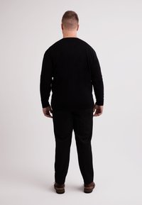 Svart långärmad tröja med rund halsringning, tillsammans med svarta byxor och bruna skor. Minimalistisk design, inga mönster eller accenter.