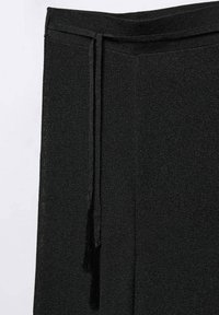 Pantalons en tricot noirs avec un tissu texturé, une taille élastique et un cordon de serrage avec des grelots, mettant en avant un design simple et fonctionnel.