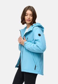 Giacca imbottita azzurro chiaro con cappuccio, chiusura con zip, due tasche laterali e patch logo nero sulla manica sinistra. Texture liscia, design casual.