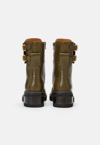 Stivaletti alla caviglia in pelle verde oliva con finitura liscia, due fibbie dorate e un tacco spesso. Presentano cuciture in vista e un dettaglio con il marchio.