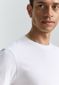 Camiseta de algodón blanca con un clásico escote redondo y mangas cortas, textura suave y diseño minimalista.