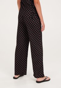 Zwarte, gemusterde broek met een relaxed fit, voorzien van een klein diamanten motief in roze. Het materiaal lijkt lichtgewicht en gestructureerd. Geschikt voor casual draag.