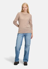 Beżowy sweter dzianinowy z długimi rękawami, okrągłym dekoltem i ściągaczami, w połączeniu z jasnoniebieskimi rozszerzanymi dżinsami i czarnymi butami na platformie.