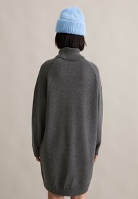 Grijze oversized trui met een hoge kraag, geribbelde zoom en verlaagde schoudernaad. Gepaard met een lichtblauwe gebreide beanie.