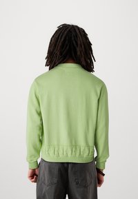 Maglione verde lavorato a maglia con scollatura rotonda e orlo testurizzato, abbinato a pantaloni grigio scuro. Presenta maniche lunghe e una vestibilità comoda.
