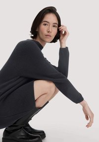 Dunkelgraues gestricktes Kleid mit hohem Kragen und langen Ärmeln, getragen mit schwarzen Lederstiefeln bis zum Knie. Weiche Textur, lockere Passform.