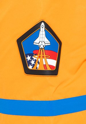 Un tessuto arancione brillante presenta una spilla esagonale nera con un disegno di uno space shuttle, accenti blu e uno sfondo con la bandiera americana.