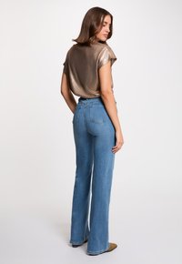 Top corto de bronce con acabado texturizado, combinado con unos vaqueros de mezclilla azul de tiro alto y campana, con bolsillos traseros cosidos y textura de mezclilla.