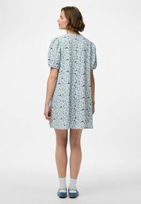 Vestido floral de color azul claro con mangas abullonadas, de longitud hasta la rodilla, que presenta patrones de flores dispersos en tonos verdes y azules, con una textura de tela suave.