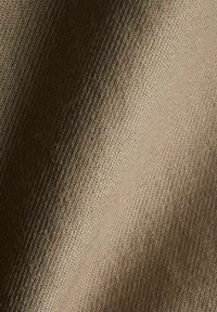 Tyg i tan med fiskbensmönster, med en mjuk textur och lätt lyster, draperad för visuell djup och dimension.