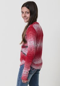 Maglione rosso a maglia con texture a gradiente; presenta un collo rotondo e maniche lunghe. Abbinato a jeans blu con cuciture decorative.