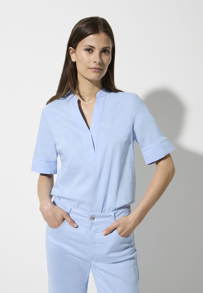 Helles blaues Kurzarm-Blusenshirt mit einem Stehkragen und einer lässigen Passform. Der Stoff wirkt glatt mit einem dezenten Glanz.