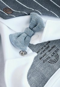 Fehér gallér kék szövetből készült masnival, szürke csíkos anyaggal és ezüst színű nyomógombbal. Texturált szürke szövet részletek és varrással kiemelt elemek.