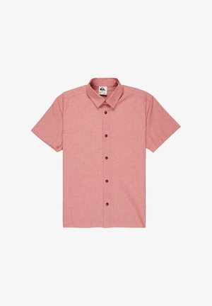 Camisa de manga corta de color rosa claro con botones marrones, combinada con pantalones cortos azul marino y zapatillas negras con detalles en verde azulado y calcetines blancos.