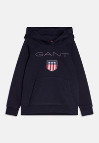 Granatowa bluza z kapturem wykonana z bawełny, z przedni�ą kieszenią, kapturem ze sznurkiem, dużym logo „GANT” oraz tarczą z czerwonymi, białymi i niebieskimi akcentami.