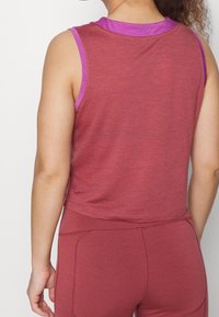 Czerwony top bez rękawów z okrągłym dekoltem, z fioletowym obszyciem i fakturowaną tkaniną. Ma krótki krój i luźne dopasowanie.