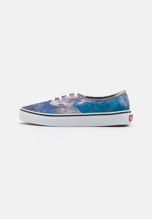Zapatilla Vans de perfil bajo con suela blanca, cordones blancos y parte superior de tela iridiscente azul-verde con etiqueta del logo de Vans en el lateral.