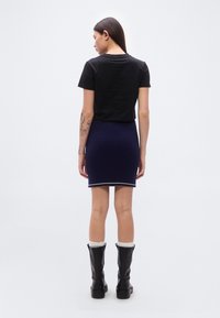 Μαύρο κοντό μπλουζάκι, ναυτικό μίνι φούστα με λευκή διακόσμηση και μαύρες μπότες μέχρι το γόνατο με λεία επιφάνεια και λευκές κάλτσες.