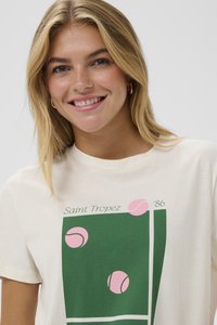 Camiseta de algodón en color crema con un gráfico verde que presenta pelotas de tenis en rosa, el texto dice "Saint Tropez '86." Mangas cortas y cuello redondo.