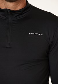 Sort langærmet træningsshirt med halvmøntkrave, der har en glat stofstruktur og "ENDURANCE" logo i hvid på brystet.