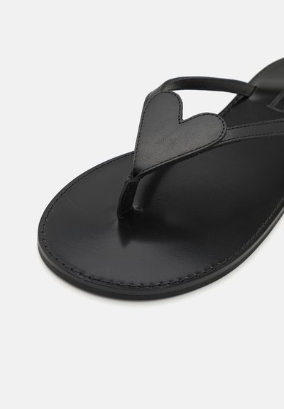 Chanclas de cuero negro con una correa en forma de corazón, textura suave y costura contorneada en la suela, diseñadas para uso casual.