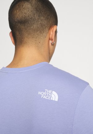 T-shirt violet clair, manches courtes, col rond, avec un logo blanc sur le haut du dos. Tissu lisse et respirant.