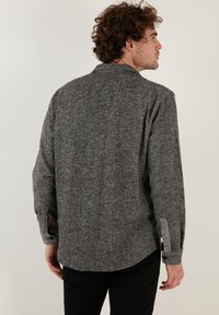 Grijs hemd met een visgraatpatroon, lange mouwen, knoopmanchetten en een kraag. De stof lijkt zacht en textuurrijk, geschikt voor casual dragen.