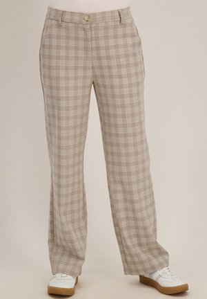 Beige en witte geruite rechte broek met knoop- en ritssluiting, gedragen met witte sneakers met rubberen zolen.