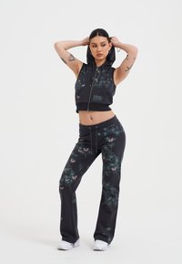 Musta vetoketjullinen lyhyt huppari kukkakuviolla, yhdistettynä samankaltaisiin mustiin housuihin, joissa on samanlaiset kuviot. Materiaali näyttää pehmeältä ja joustavalta.