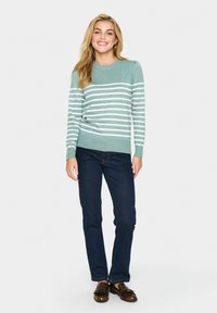 Lichtblauwe trui met witte strepen, ronde hals en geribbelde manchetten, gecombineerd met donkere jeans en bruine schoenen. Soepele stoftextuur.