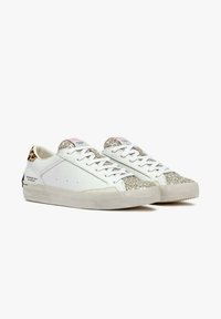 Zapatillas blancas con una puntera texturizada y brillante, acentos de estampado de leopardo en el talón y cordones planos. Suela de goma con un dibujo mínimo.