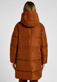 Brun oppustelig jakke med hætte, med lodrette syede paneler, en mid længde design og en glat, shiny tekstur.